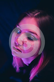 A beautiful young woman, adorned with star-shaped makeup, in a club illuminated by pink lights amidst the darkness of the night