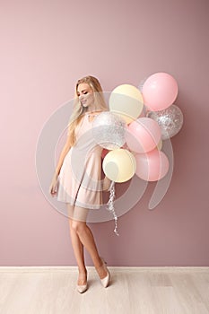 Beautiful young woman with air balloons against color wall