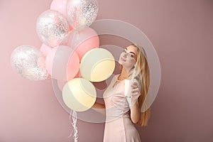 Beautiful young woman with air balloons and cocktail on color background