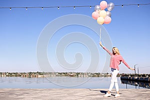 Beautiful young woman with air balloons near river