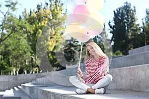 Beautiful young woman with air balloons sitting on stairs outdoors
