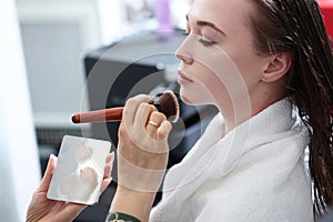 A beautiful young woman applies blush to her face with a makeup brush. Professional makeup in a beauty salon. Form