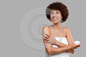 Beautiful young woman applying body cream onto arm on grey background, space for text