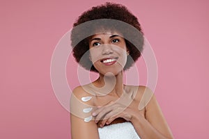 Beautiful young woman applying body cream onto arm on pink background