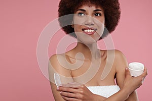 Beautiful young woman applying body cream onto arm on pink background, space for text