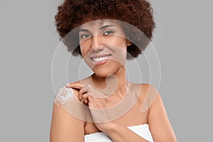 Beautiful young woman applying body cream onto shoulder on grey background