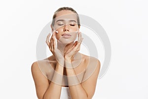 Beautiful young woman applying cosmetic cream treatment on her face isolated on white background