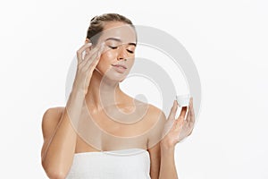 Beautiful young woman applying cosmetic cream treatment on her face isolated on white background