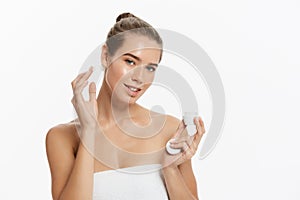 Beautiful young woman applying cosmetic cream treatment on her face isolated on white background