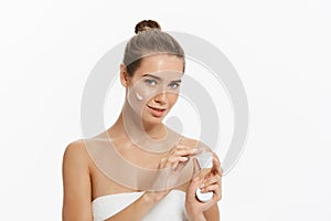 Beautiful young woman applying cosmetic cream treatment on her face isolated on white background