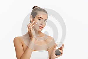 Beautiful young woman applying cosmetic cream treatment on her face isolated on white background