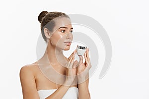 Beautiful young woman applying cosmetic cream treatment on her face isolated on white background