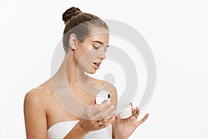 Beautiful young woman applying cosmetic cream treatment on her face isolated on white background
