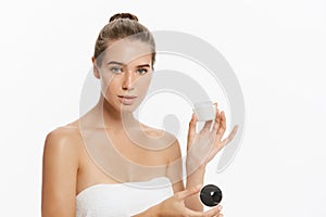 Beautiful young woman applying cosmetic cream treatment on her face isolated on white background