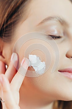 Beautiful young woman applying cream on the cheek. Face Skin care concept