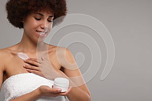 Beautiful young woman applying cream onto body on grey background, space for text