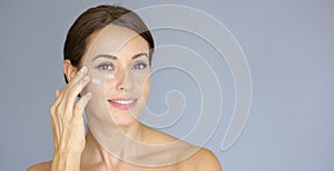Beautiful young woman applying face cream photo