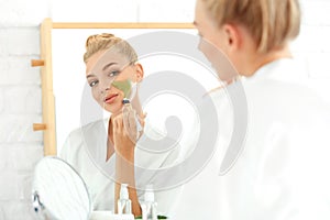 Beautiful young woman applying facial mask with aloe vera extract at home