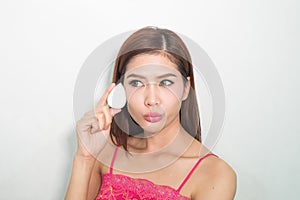 Beautiful young woman applying foundation to face with green egg