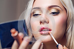 Beautiful young woman applying lips makeup with cosmetic brush