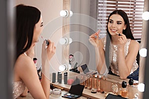 Beautiful young woman applying makeup near mirror in room