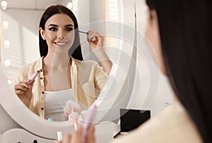 Beautiful young woman applying makeup near mirror