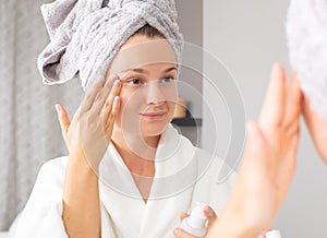 Beautiful young woman applying moisturizer on face