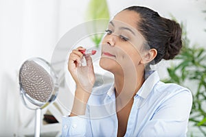 Beautiful young woman applying scarlet lipstick