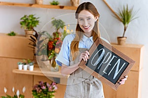 beautiful young woman in apron holding sign open and smiling at camera