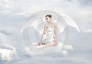 Beautiful young woman as angel sitting on a cloud