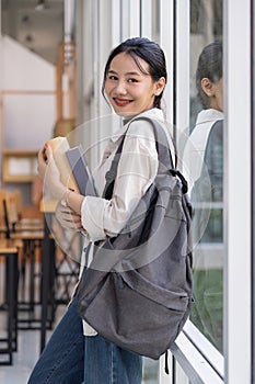 Beautiful young woman asian with backpack and book. College student carrying lots of books in college campus