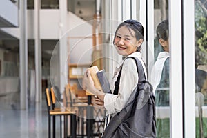 Beautiful young woman asian with backpack and book. College student carrying lots of books in college campus