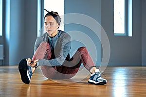 Beautiful young woman athlete tying shoelaces on sneakers while relaxing from strength training in the gym. oncept of