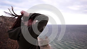 A beautiful young woman athlete walks to the edge of a cliff on a windy day. Sports sweatshirt, strong wind disheveles