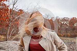 Beautiful young woman in autumn park. Face hidden behind hair, wind blowing hair of beautiful girl outdoor