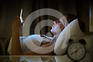 Beautiful young woman awake using smartphone in bedroom at night. Mobile phone abuse concept.