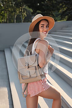 Beautiful young woman with backpack and hat on stairs outdoors