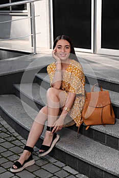 Beautiful young woman with backpack sitting on stairs outdoors