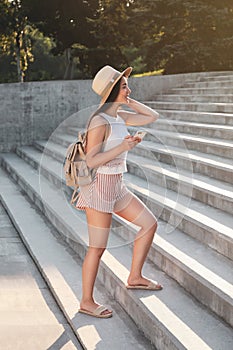 Beautiful young woman with backpack and smartphone walking up stairs outdoors