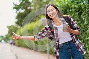 beautiful young woman with a backpack uses a phone while hailing a car to travel