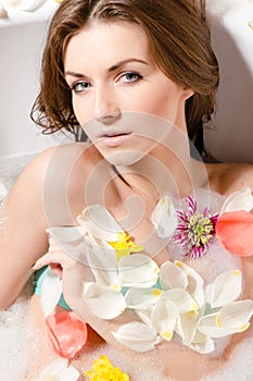 Beautiful young woman in bath with flower petals