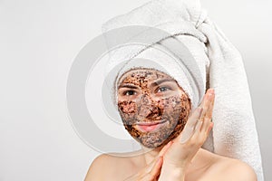 A beautiful young woman with a bath towel on her head and a coffee mask on her face takes care of her skin
