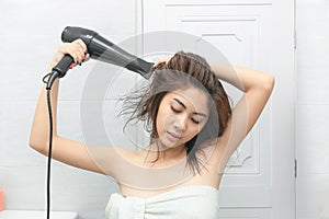 Beautiful young woman in bath towel is using a hair dryer