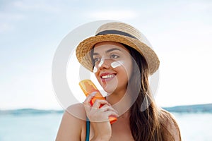Beautiful young woman at beach applying sunscreen on face and looking at camera. Beauty girl applying suntan lotion at sea.