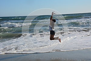 Beautiful young woman on the beach jumping for joy