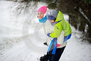 Beautiful young woman bears on the son`s shoulders through snowdrifts.