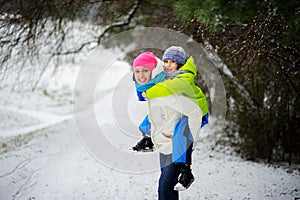 Beautiful young woman bears on the son`s shoulders through snowdrifts.