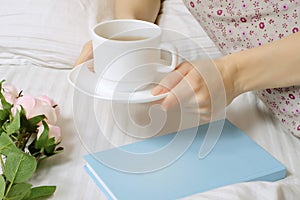 Beautiful young woman in bed drinking tea reading book