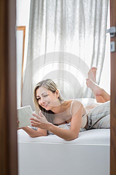 Beautiful young woman in bed, using her tablet computer