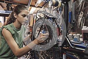 A beautiful young woman bicycle mechanic is repairing a bike in the workshop